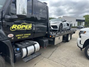 A Roper Automotive and Towing LLC flatbed tow truck loading a white sports car in Greenville, SC.