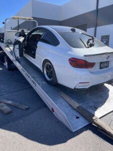 A C&B Towing flatbed truck loading a white BMW coupe using wooden ramps in Mesa, AZ.