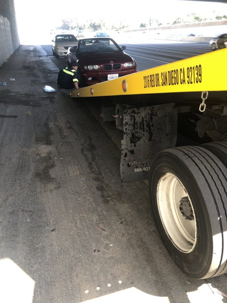 A Ledesma's Towing operator assisting a red convertible car under an overpass in San Diego, CA.