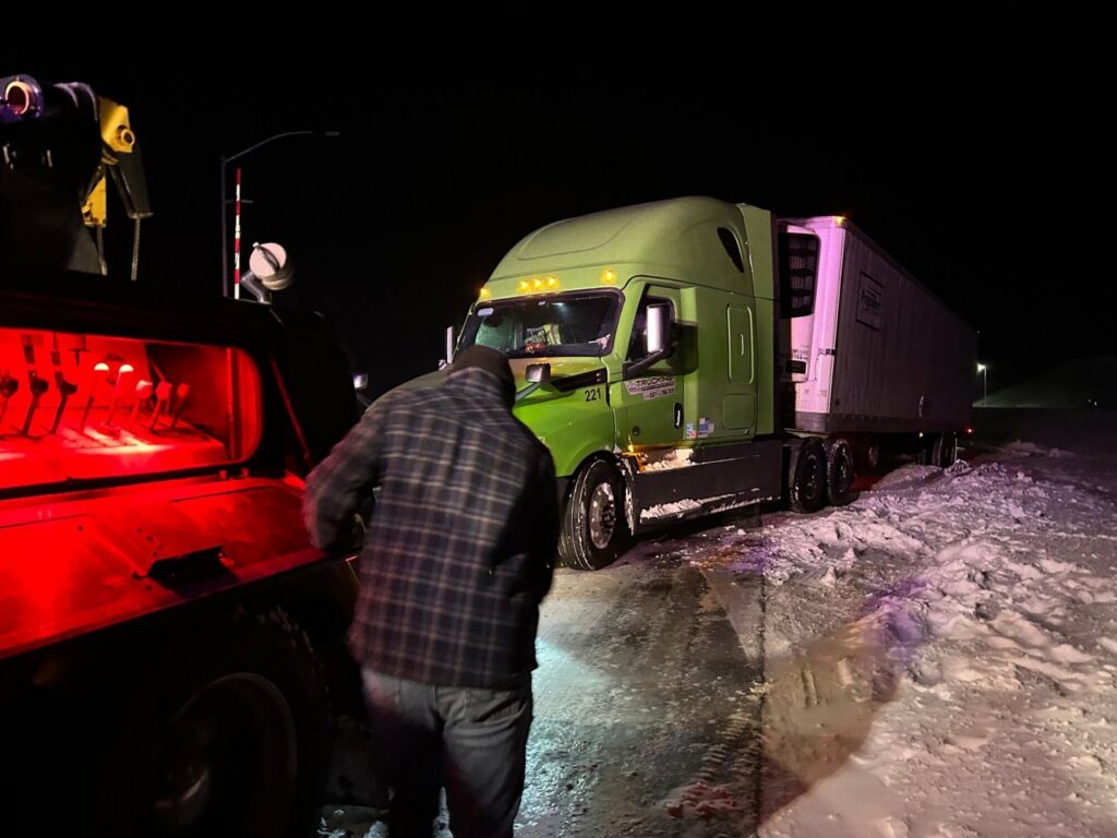 A tow truck operator from Select Towing and Recovery assisting a semi-truck stuck in snow at night in Casper, WY.