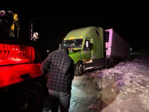 A tow truck operator from Select Towing and Recovery assisting a semi-truck stuck in snow at night in Casper, WY.