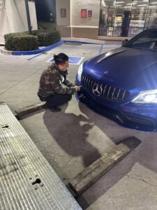 A tow truck operator from Leos Towing Service attaching a hook to a blue Mercedes-Benz sedan in Anaheim, CA.