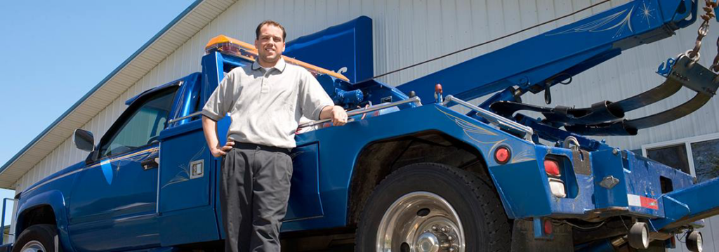 A friendly tow truck operator standing proudly next to a blue tow truck from Tows R Us in Scottsdale, AZ.