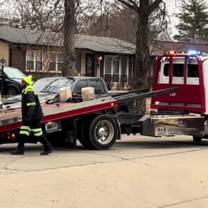 A tow truck operator in a high-visibility vest loading a dark car onto a flatbed for Columbus Towing in Columbus, GA.