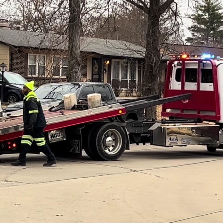 A tow truck operator in a high-visibility vest loading a dark car onto a flatbed for Columbus Towing in Columbus, GA.