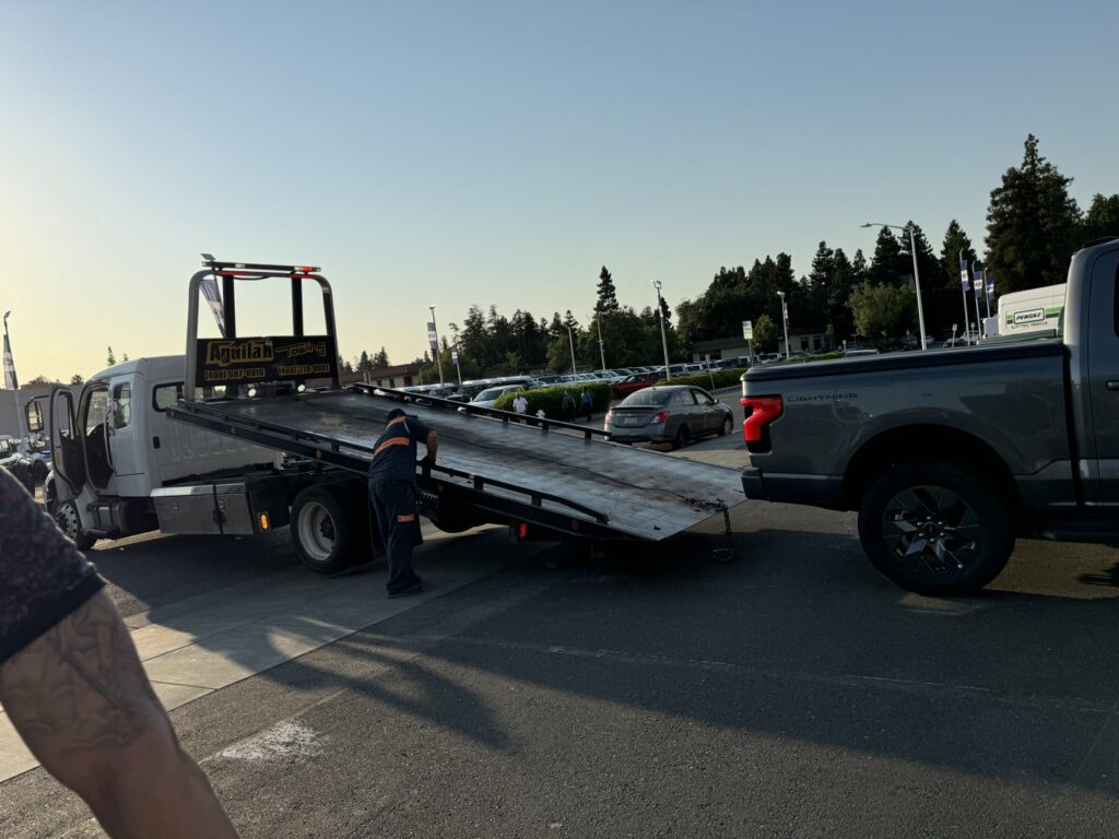 An Aguilar Towing operator preparing to load a grey pickup truck onto a flatbed tow truck in San Jose, CA