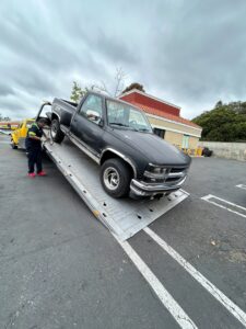 A Ledesma's Towing operator loading a black pickup truck onto a flatbed tow truck in San Diego, CA.