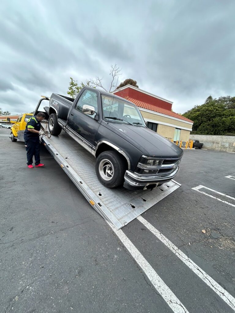 A Ledesma's Towing operator loading a black pickup truck onto a flatbed tow truck in San Diego, CA.