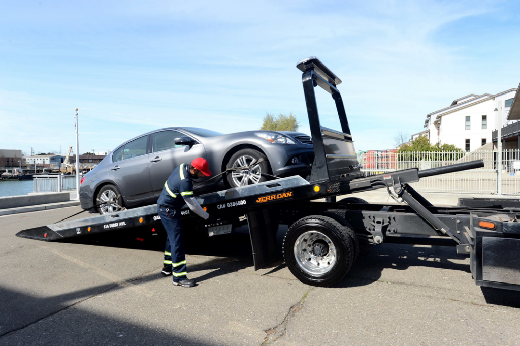 A tow truck operator loading a grey sedan onto a flatbed tow truck for Emergency Towing San Francisco in San Francisco, CA.