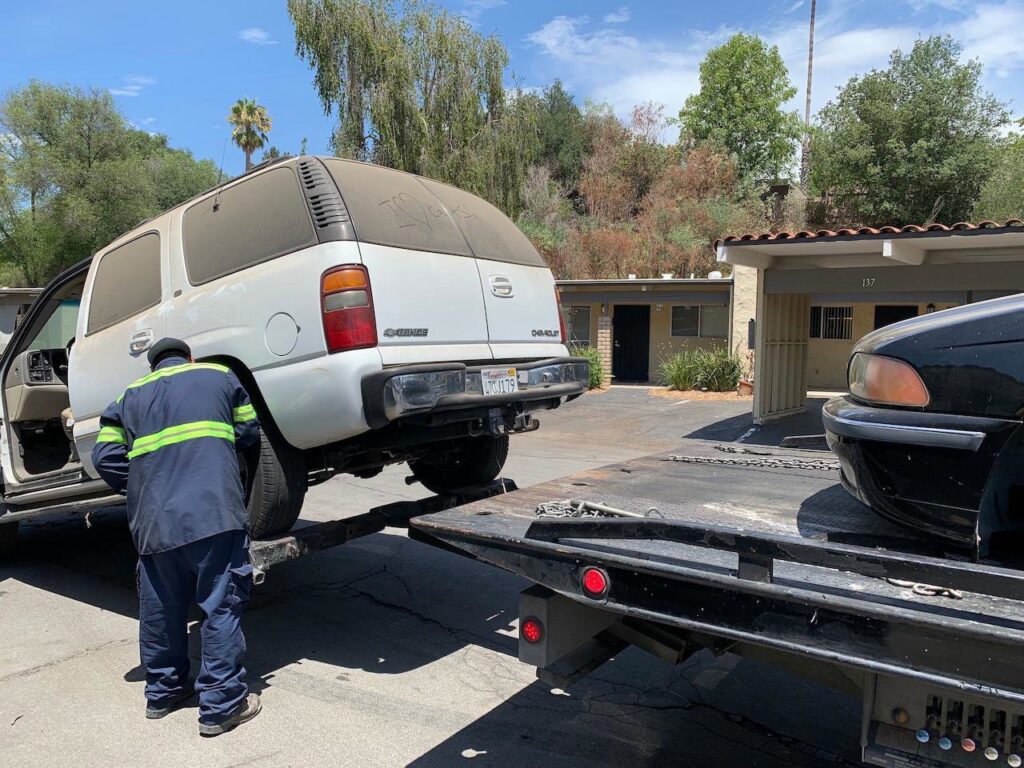 A tow truck operator from All Roadside Towing San Diego, CA, loading a white SUV onto a flatbed.