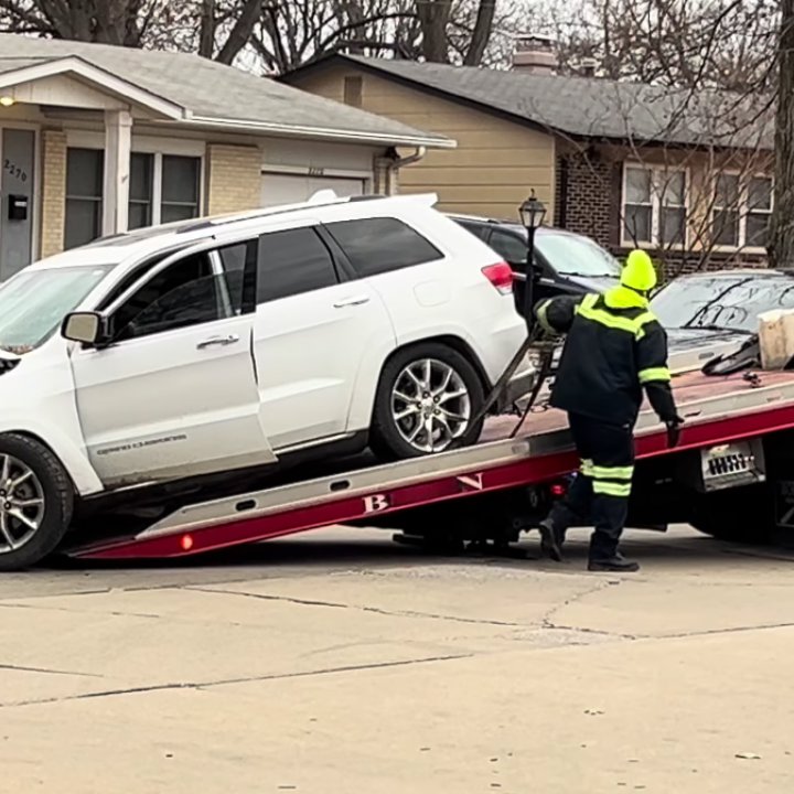 A tow truck operator in a high-visibility vest loading a white SUV onto a flatbed for Columbus Towing in Columbus, GA.