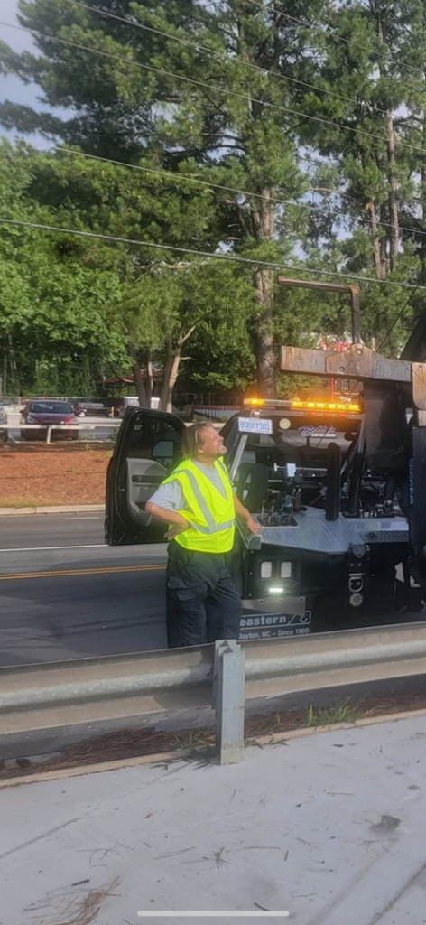 A Bobbys Towing & Recovery operator in a high-visibility vest on a job site with a wrecker tow truck in Raleigh, NC.
