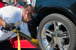 A tow truck operator securing a black car's wheel with a strap on a flatbed for Spokane Towing Services in Spokane, WA.