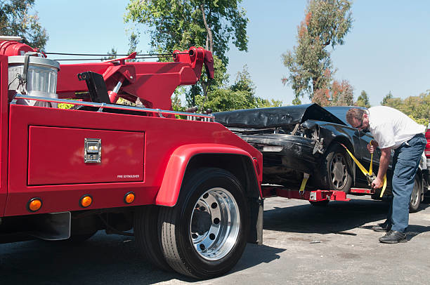 A tow truck operator securing a heavily damaged black car onto a red tow truck for Jensen Towing in Kenosha, WI.