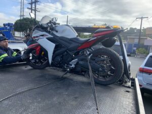 A tow truck operator from All Roadside Towing San Diego, CA, securing a motorcycle onto a flatbed.