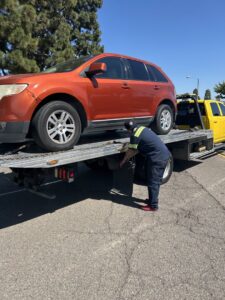 A Ledesma's Towing operator securing an orange SUV onto a flatbed tow truck in San Diego, CA.