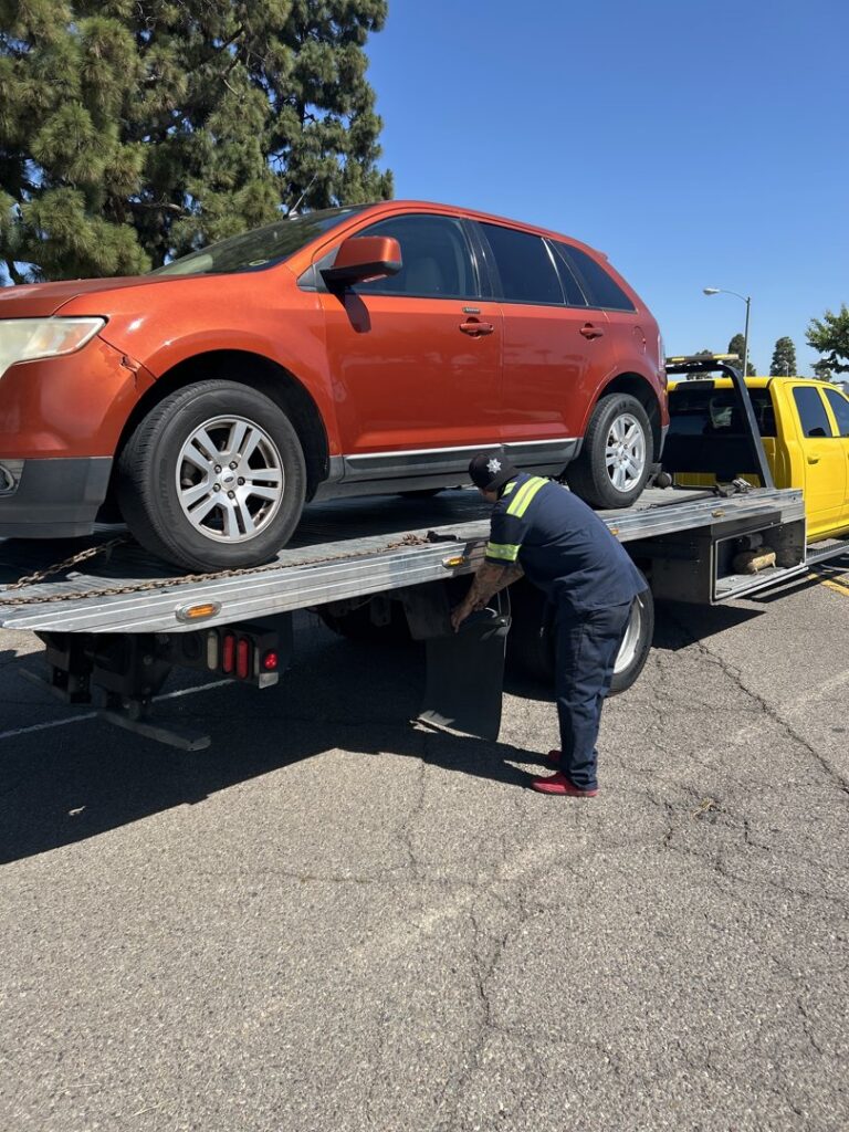 A Ledesma's Towing operator securing an orange SUV onto a flatbed tow truck in San Diego, CA.