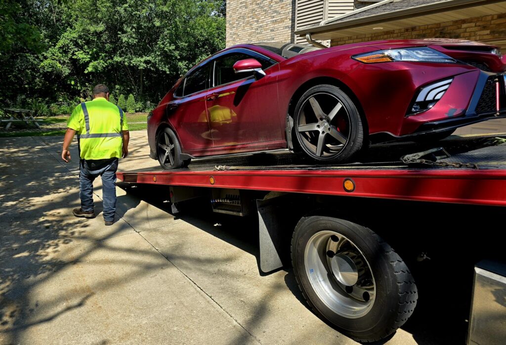 A tow truck operator walking alongside a red car loaded onto a flatbed tow truck by Jensen Towing in Kenosha, WI.