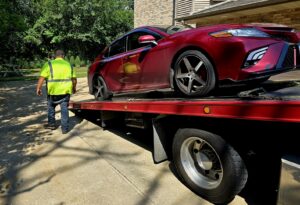 A tow truck operator walking alongside a red car loaded onto a flatbed tow truck by Jensen Towing in Kenosha, WI.