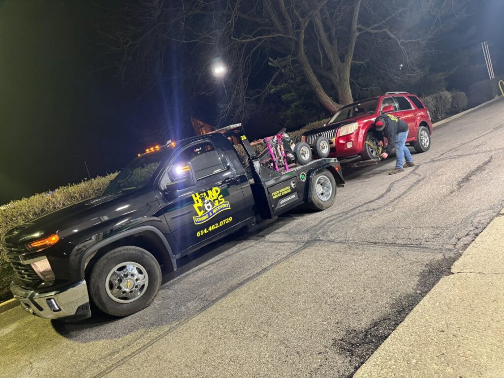 A Hound Dog's Towing & Recovery tow truck preparing to tow a red SUV with a worker in Columbus, OH.