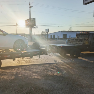 A tow truck pulling a trailer with a white car on it by Mountain Goat Rescue & Recovery LLC + Towing in Nampa, ID.