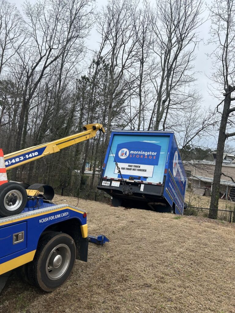 A yellow and blue tow truck from Andre's Towing Services, LLC recovering a box truck from a ditch in Marietta, GA.