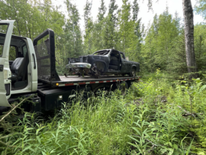 A Solid Choice Towing flatbed truck recovering a damaged vehicle from a wooded area, offering services in Wasilla, AK.