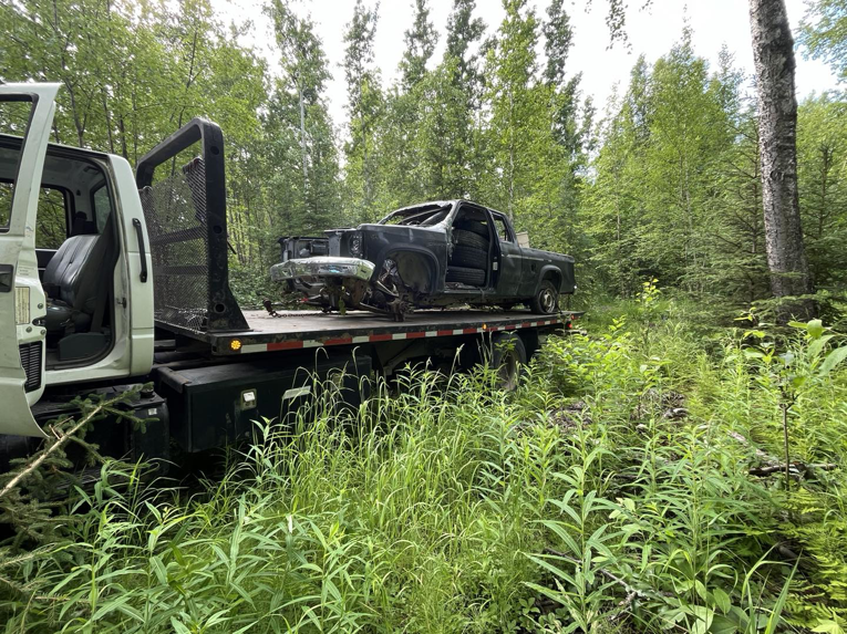 A Solid Choice Towing flatbed truck recovering a damaged vehicle from a wooded area, offering services in Wasilla, AK.