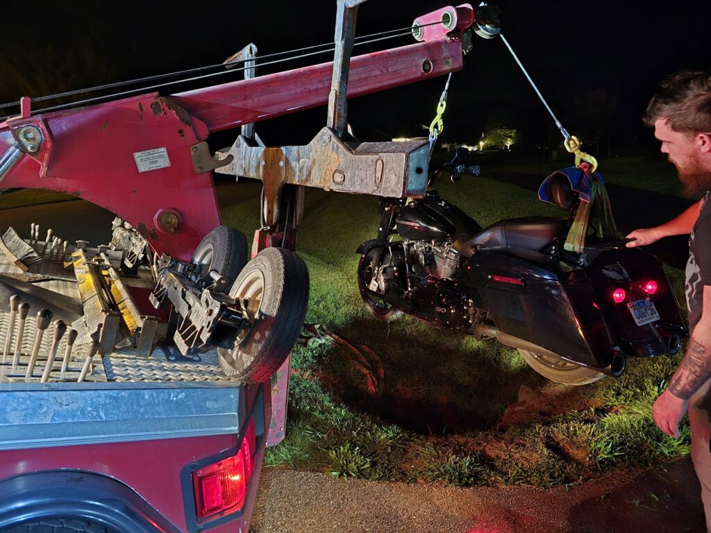 A red tow truck is recovering a motorcycle from a ditch with assistance from a person for A and D Towing in Little Ferry, NJ.