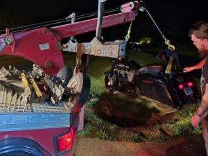 A red tow truck is recovering a motorcycle from a ditch with assistance from a person for A and D Towing in Little Ferry, NJ.