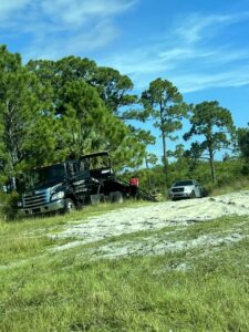 A black tow truck from Always Ready Towing recovering a white pickup truck from a ditch in North Fort Myers, FL.