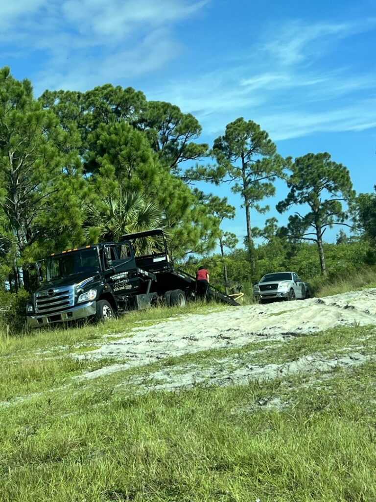 A black tow truck from Always Ready Towing recovering a white pickup truck from a ditch in North Fort Myers, FL.