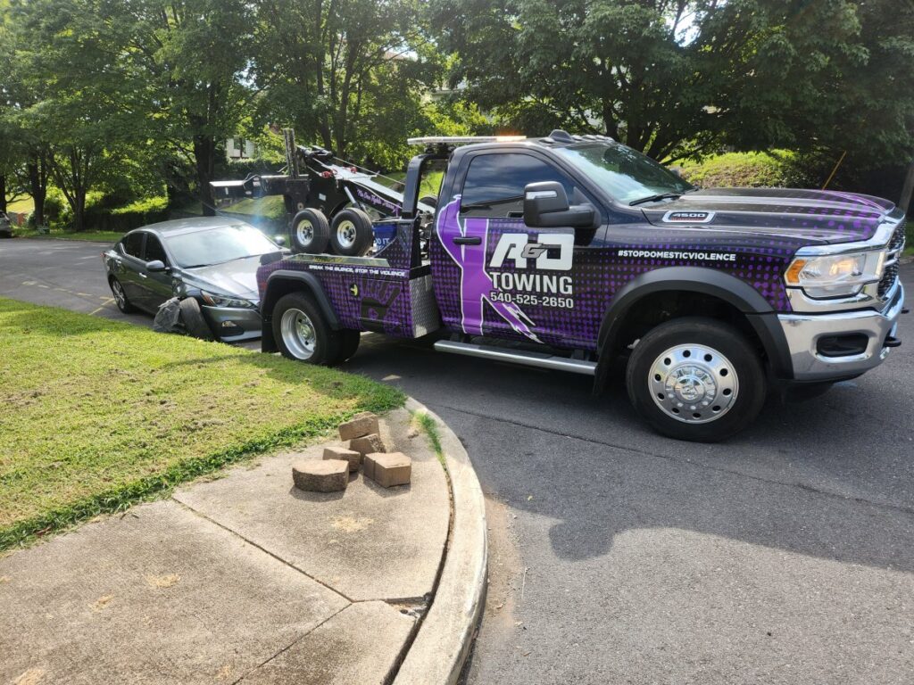 A purple A and D Towing truck is recovering a grey sedan from a ditch in Little Ferry, NJ.