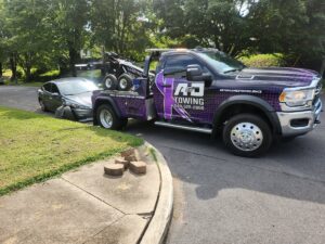 A purple A and D Towing truck is recovering a grey sedan from a ditch in Little Ferry, NJ.