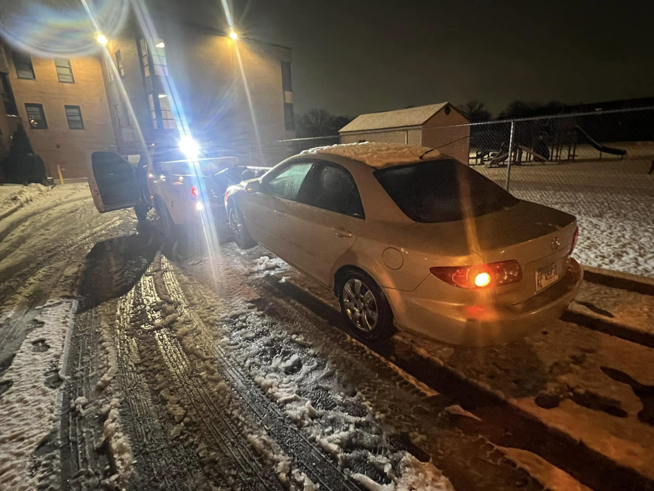 A Trevi Towing llc truck recovering a light-colored sedan from snow at night in Chicago, IL.