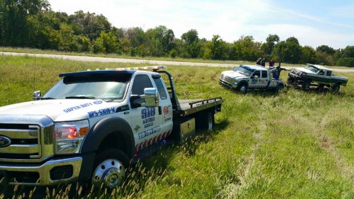 A 918 Wrecker Service tow truck on a recovery job in a grassy area, assisting another vehicle in Tulsa, OK.