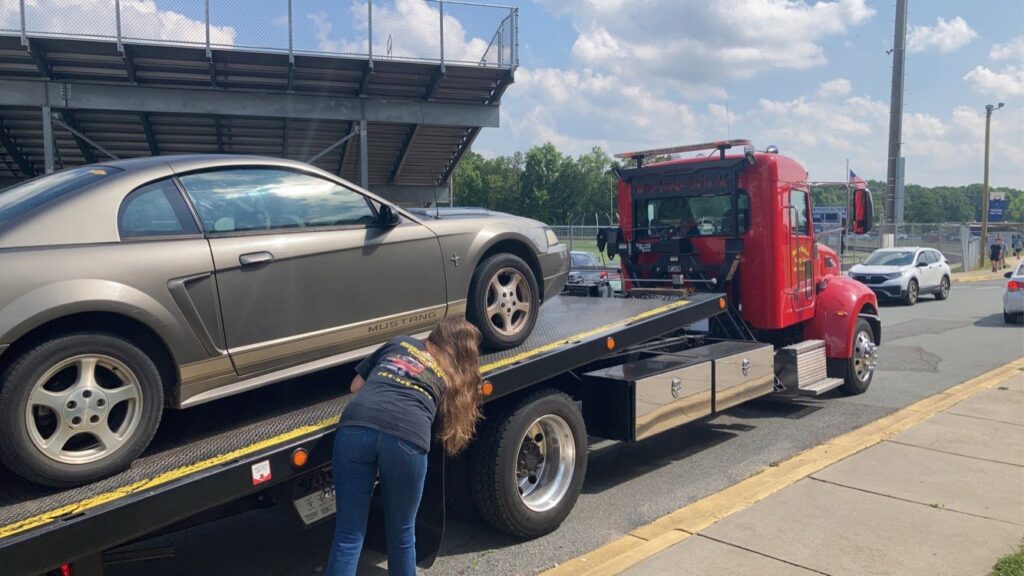 A red flatbed tow truck from Rubber Chicken Towing LLC securing a grey Ford Mustang onto its bed in Charlotte, NC.