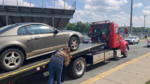 A red flatbed tow truck from Rubber Chicken Towing LLC securing a grey Ford Mustang onto its bed in Charlotte, NC.