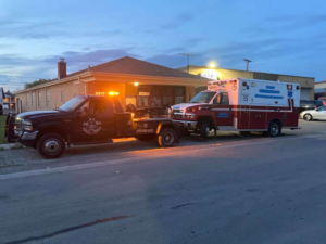 An O.T.W Towing & Recovery LLC tow truck actively towing an ambulance at dusk in Chicago, IL.