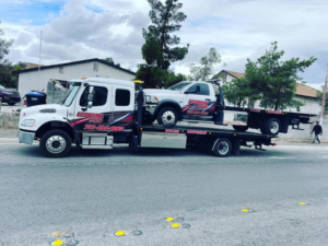 A large Economy Towing flatbed truck towing a smaller Economy Towing flatbed truck in Las Vegas, NV.