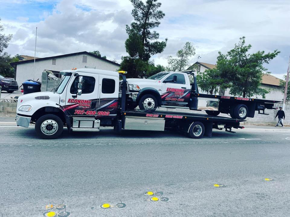 A large Economy Towing flatbed truck towing a smaller Economy Towing flatbed truck in Las Vegas, NV.