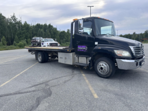 A Solid Choice Towing flatbed truck transporting another tow truck, showcasing diverse towing capabilities in Wasilla, AK.