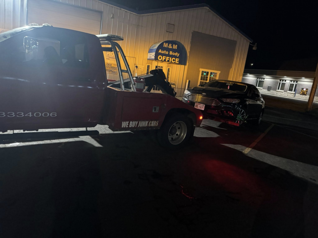 A PNB towing truck actively towing a black car at night in Madison, WI.