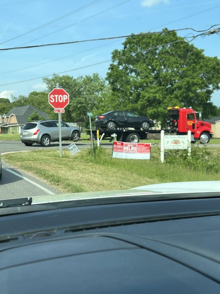A red flatbed tow truck from Rubber Chicken Towing LLC towing a black car on a road in Charlotte, NC.