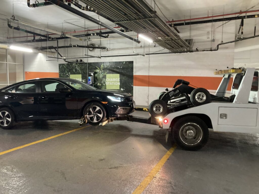 An E.C. Towing, Inc. tow truck towing a black car in an indoor parking garage in Gaithersburg, MD.