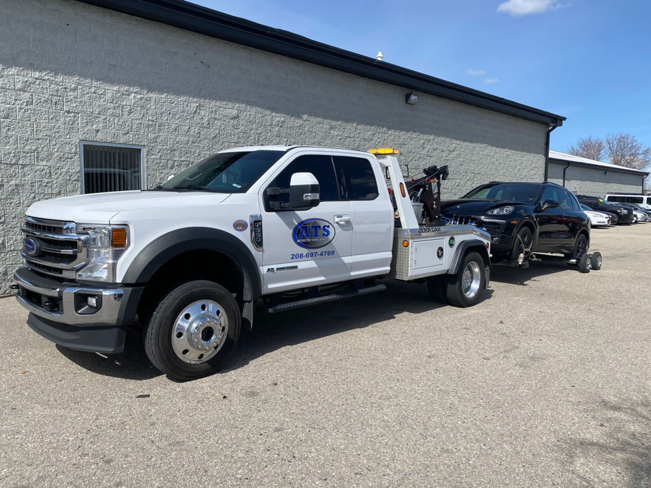 A white tow truck from Automotive Technical Services towing a black SUV in Boise, ID.
