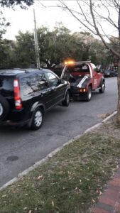 A red tow truck from Savannah Towing And Recovery actively towing a black SUV on a street in Savannah, GA.