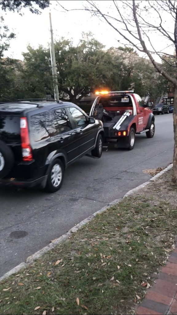A red tow truck from Savannah Towing And Recovery actively towing a black SUV on a street in Savannah, GA.