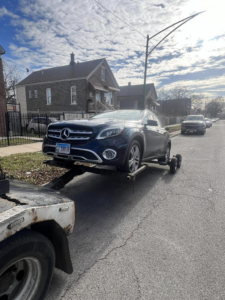 A Trevi Towing llc truck towing a dark blue SUV with a dolly on a street in Chicago, IL.