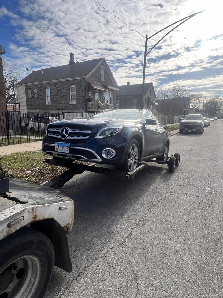 A Trevi Towing llc truck towing a dark blue SUV with a dolly on a street in Chicago, IL.
